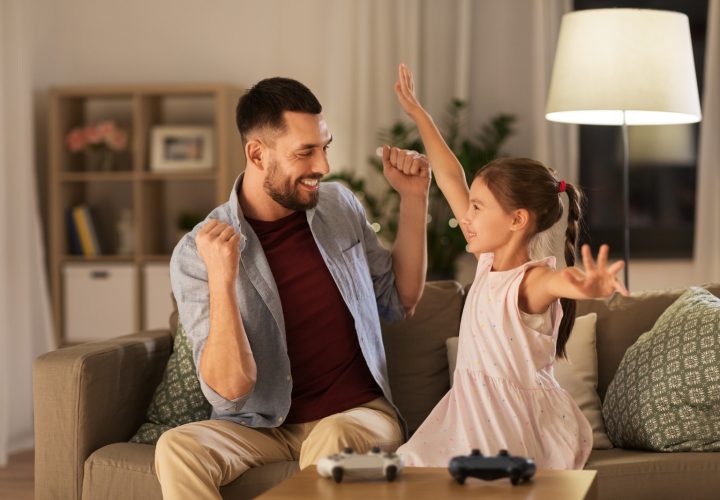 family, gaming and entertainment concept - happy father and little daughter with gamepads celebrating triumph in video game playing at home